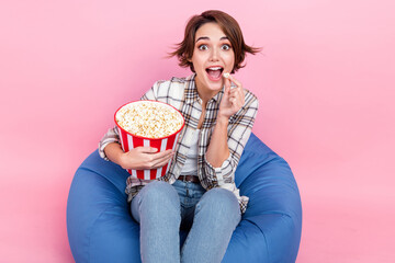 Photo of astonished pretty girl sit comfort bag eat popcorn watch new movie isolated on pink color...