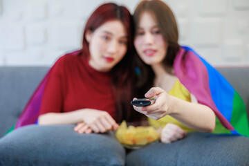 Female couple enjoying time together on a sofa. watching the television with a bowl of snack.