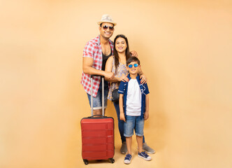 Young Indian family with trolley bag luggage going for summer vacations isolated over beige...