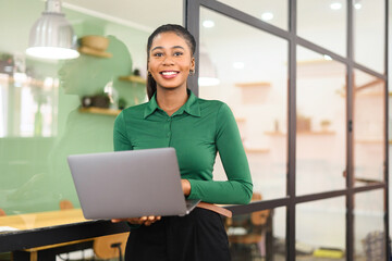 Inspired businesswoman in smart casual wear using laptop standing at the coworking, smiling female office employee looking at the camera indoors, woman with laptop computer at office