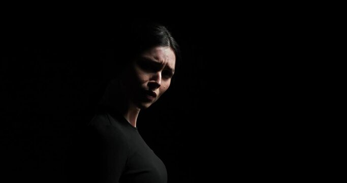 woman standing in profile against a black background. She quickly raises her head, looks directly into the camera, and have deep breath. She feel distress, sadness, and anger.