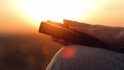 Close-up of a Bible in a woman's hands at sunset. Christianity