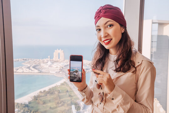Indian girl travel blogger taking photos on her smartphone from height of a rooftop viewpoint on skyscraper in Abu Dhabi, UAE