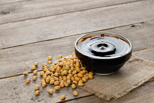 soy sauce in glass bowl with falling drops and dry soybeans on table
