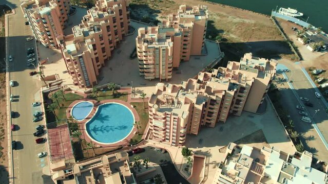 Aerial shot, drone point of view of La Manga del Mar Menor residential buildings exterior and swimming pool during sunny summer day. Travel and tourism concept. Murcia, Costa Calida. Spain
