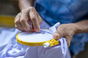 Close-up view. Hand of an elderly Thai woman using a slitting needle to pull the old blue thread.