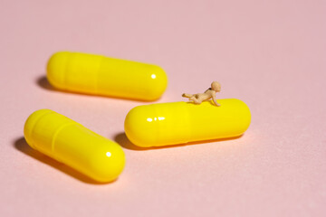 Miniature tiny people toy figure photography. A newborn baby crawling above yellow medicine pill tablet. Isolated on pink background