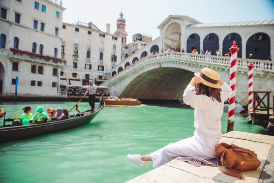 woman sitting near rialto bridge in venice italy looking at grand canal with gondolas