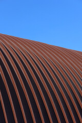 The roof of the hangar is made of stainless steel. The arched roof is made of metal construction. An industrial building in detail against a blue sky background. Construction. Vertical snapshot