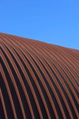 The roof of the hangar is made of stainless steel. The arched roof is made of metal construction. An industrial building in detail against a blue sky background. Construction. Vertical snapshot © Elena