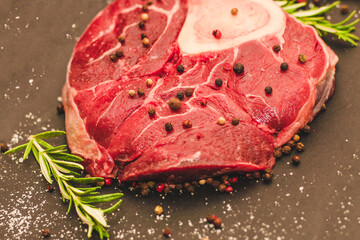 Fresh piece of meat large beef steak on the bone ossobuco with a sprig of rosemary on a black background.
