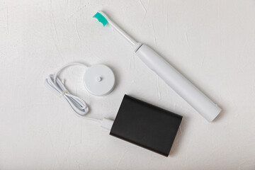 A modern electric toothbrush is being charged from an external power bank battery on a marble background. Modern home technology concept. Oral and gum care. Medicine concept. Dentist.