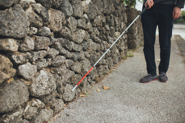 白杖を持った視覚障害者の男性が沖縄で石垣の近くを歩いている