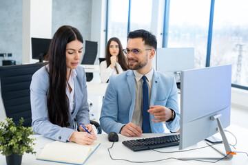 Handsome businessman confidently giving instructions to his female colleague, who diligently taking...