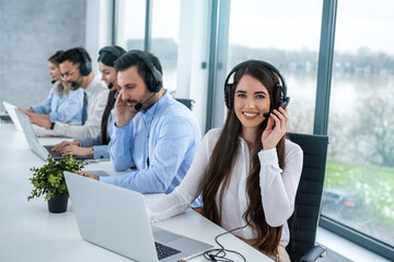 Call center agent woman with headset working on support hotline in modern office with group of...