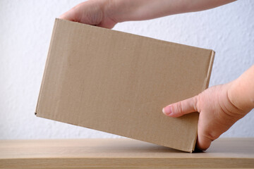 Obraz premium close-up of female hands open cardboard box of medium size stands on wooden stool, postal box with wrapping paper, a parcel, delivery of ordered goods, online shopping, timely delivery to customers