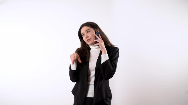 Engaged young female with expressive body language in formal wear with dark hair against white background talking on her smartphone and finishing the call 