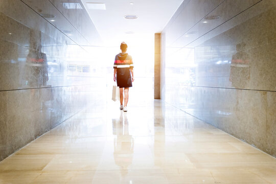 Woman Walking Down A Corridor Towards Lit Exit