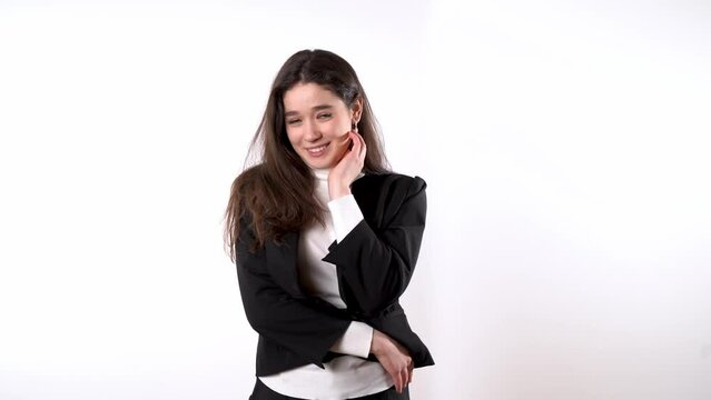 Elegantly dressed young lady with long dark hair against white background smiling coquettishly while provocatively stroking her chin