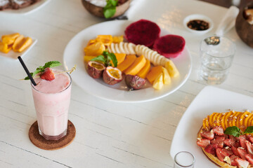 Glass of strawberry milkshake on cafe table next to plate of fresh cut fruits