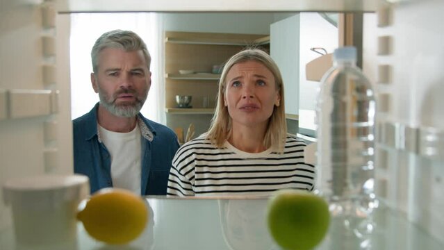 Point Of View POV From Inside Refrigerator Caucasian Adult Couple Open Empty Fridge Woman Sad Despair With Lemon Apple Bottle Of Water Family Middle-aged Husband And Woman Need Shopping Food Delivery