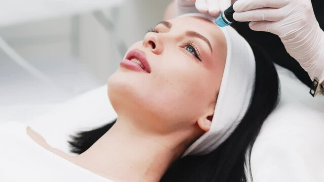 Professional qualified beautician standing next to client during hydrafacial procedure. Pleasant beauty procedure. Joyful positive woman smiling while enjoying the beauty procedure