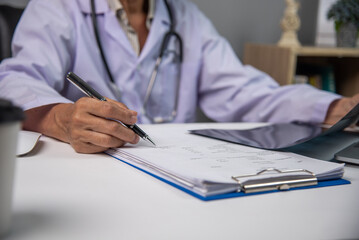 Fototapeta premium Female doctor holding a pen writing patient medical papers on clipboard and looking at x-ray film