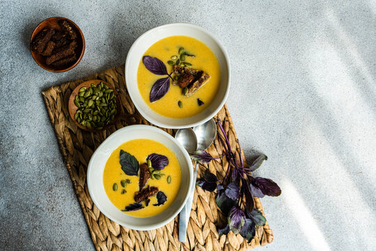 Bowls with pumpkin cream soup with basil herb on table