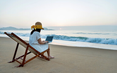 Woman sitting on beach and working with laptop.