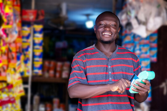 A black african man standing in front of a store holding a pos machine