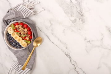 Bowl of oat granola with yogurt, fresh raspberries, blueberries, strawberries, banana and nuts with spoon on white background for healthy breakfast. Top view. Copy space