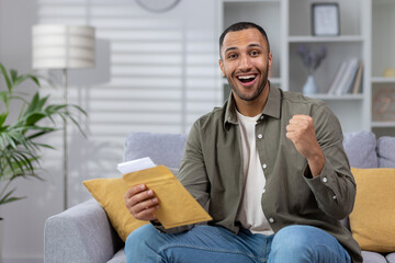 Portrait of happy young African American male student receiving good news from university. Holds a...