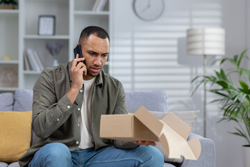 A frustrated African American young man at home talks on the phone with the delivery service,...