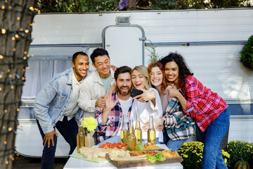 Mixed race friends taking selfie on mobile phone, outdoor party on travel trailer background. Rest outside the city. Happy people enjoy. Weekends in the summer time.