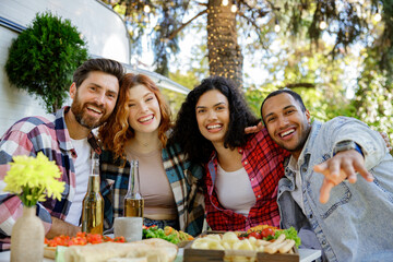 A group of friends are relaxing in nature. Two girls and two boys of different races are looking at the camera, smiling, having fun on the background of a travel trailer.
