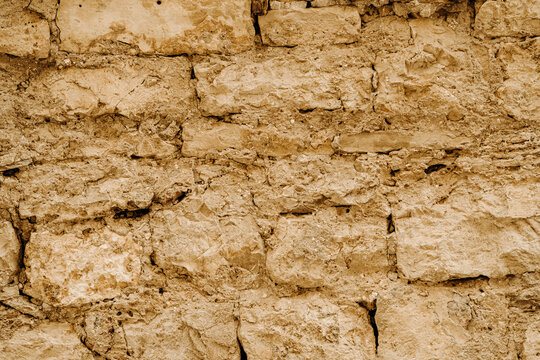 horizontal texture of old wall made of coarse brown sandstone, with cracked old plaster made of clay