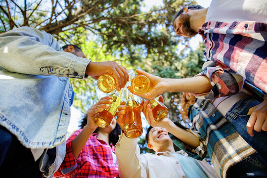 A cheerful multinational company is having fun on a picnic. Multisex friends sitting at the table outdoors celebrating eating and drinking drinks.