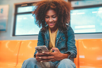 Happy young African American woman passenger smile and using smart mobile phone in subway train station. - obrazy, fototapety, plakaty