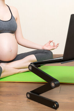 Young happy healthy yoga fitness beautiful pregnant woman doing bakasana yoga workout on yoga mat opposite laptop with online master class. lifestyle concept at coronavirus time