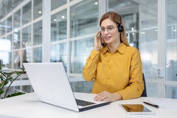 Portrait of a young woman in a headset working in an office center online from a laptop.