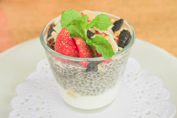 Close-up top view photo fruit pudding with various toppings such as mint leaves, strawberries, raisins, sliced ​​almonds and chia seeds. Concept for healthy eating, fat loss, organic food, vegan diet.