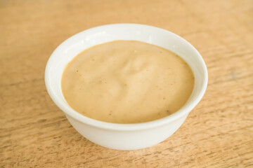 Roasted sesame dressing in the small white round bowl isolated on wooden background. Salad dressing, sauce, mayonnaise, oil. Copy text blank empty space - Close up photo.