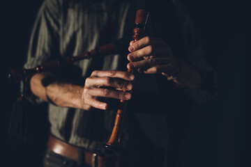 Bagpipe player playing his instrument in an auditorium with stage lights and a black background. 