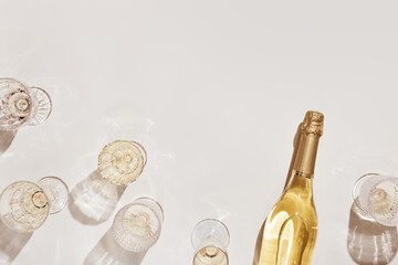Flat lay with white sparkling wine bottle, set glasses wine with sunshine shadow and flare on light...