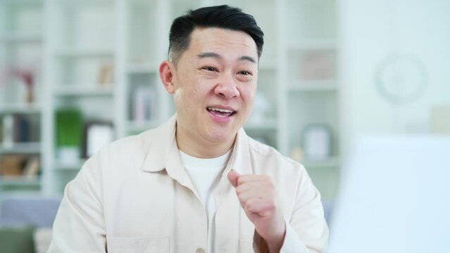 Close up. Confident asian businessman talking on video call on laptop while sitting in home office. A smiling coach or tutor conducts an online training, seminar, training, course or webinar remotely