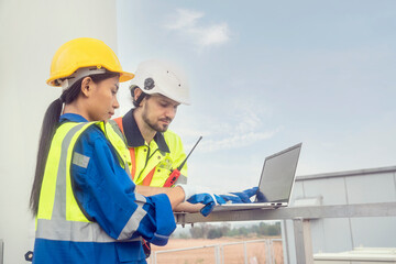 One male engineers and a female foreman team stand at the wind turbine station and talk toplanning work to inspect and repair wind turbines to produce electricity working with laptop at the station of