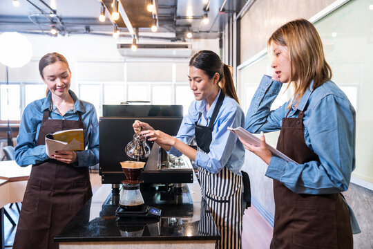 Barita girl grinding coffee and roasting coffee with a coffee machine trains new employee training. Two girls take notes at the counter in a coffee sho