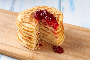Pancakes with red berry jam on the wooden table.