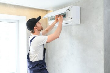 Smiling young male electrician repair conditioner in client home. Man mechanic or repairman fix filters in air condition device at customer house