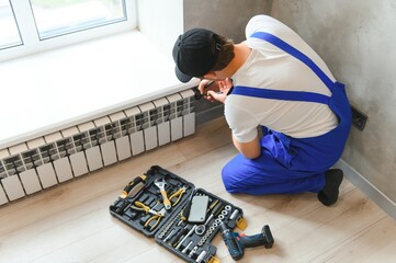 heating system installation and maintenance service. plumber installing radiator.